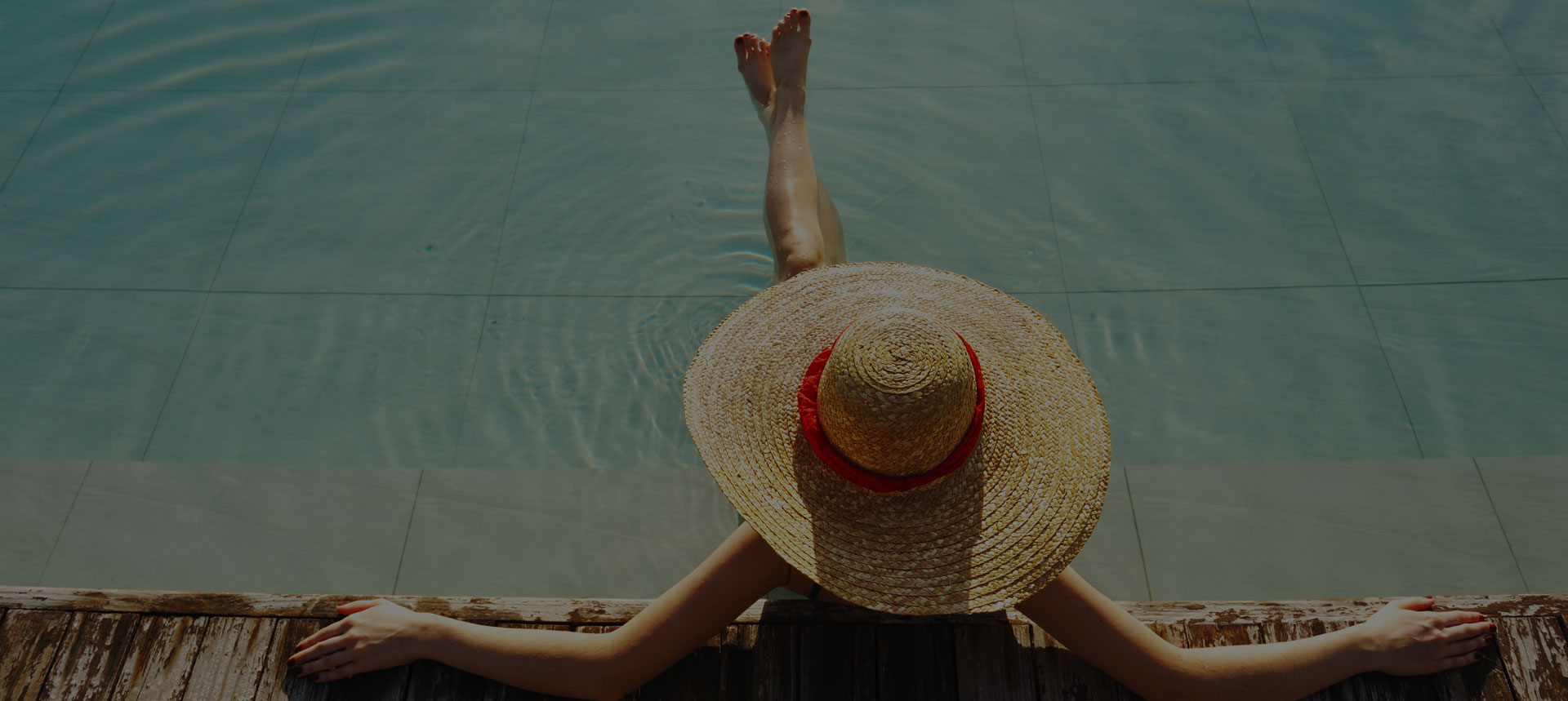 Woman with a straw hat sitting by a pool.
